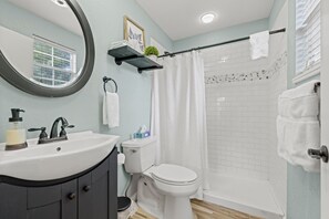 A bathroom with a white sink, a toilet, a shower with a glass door, and a towel rack. - Columbus Cottage, .5 Miles to Main, Private Hot Tub! (Fredericksburg)