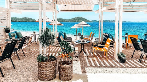 Een terras met tafels, stoelen, parasols en plantenpotten.
