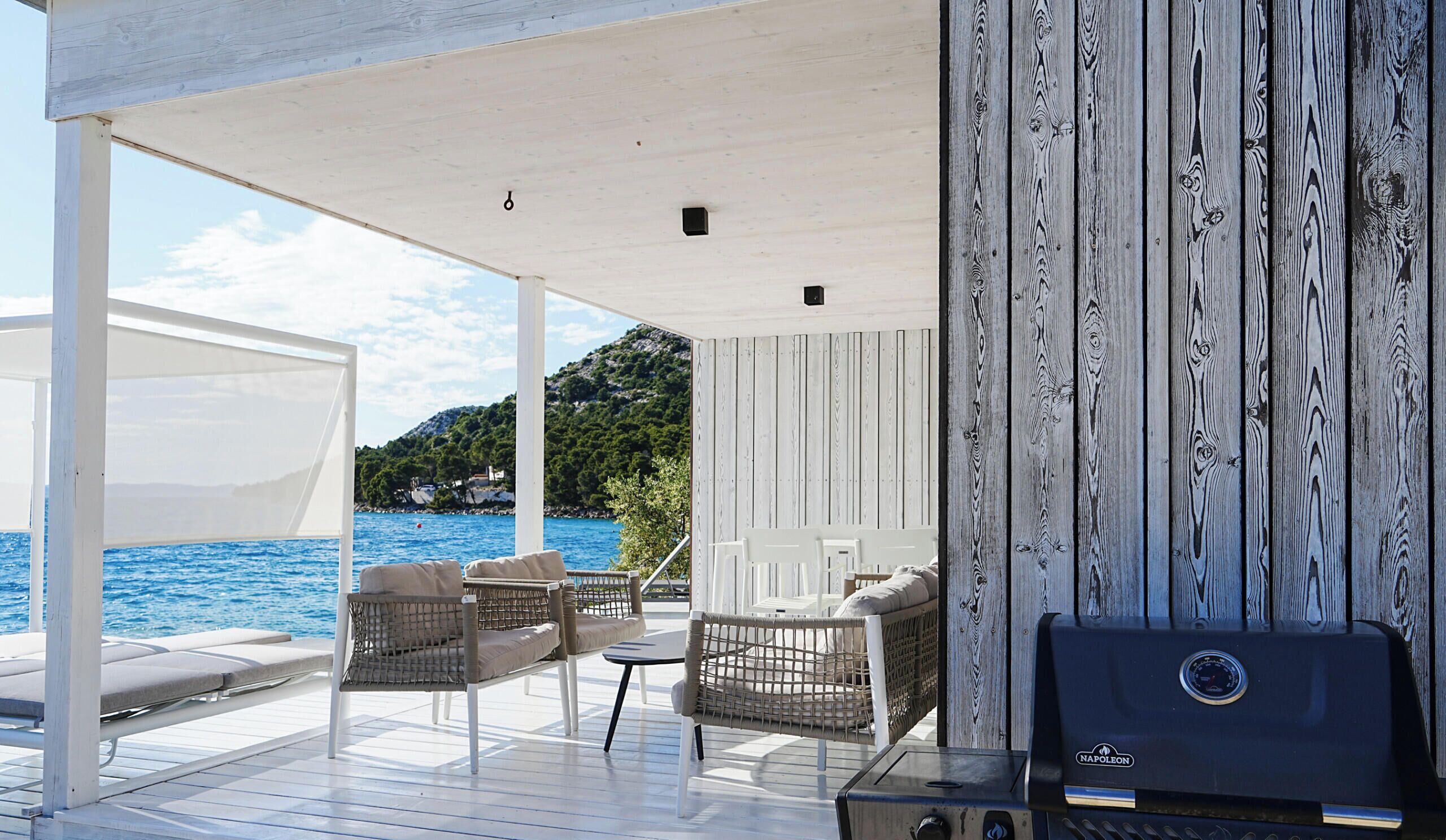 Un espacio al aire libre techado con mobiliario de mimbre, una parrilla y vistas al mar y las colinas.