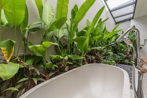 Bathroom features a bathtub surrounded by lush greenery.