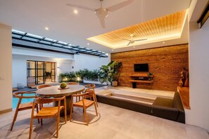 Relax in this open-plan living space with a high ceiling, featuring a dining area, bench, and flat-screen TV.