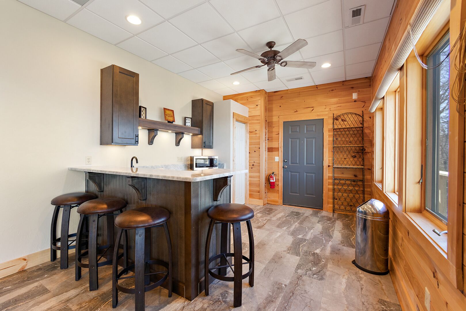 A kitchen with a bar area, wooden walls, and a ceiling fan.