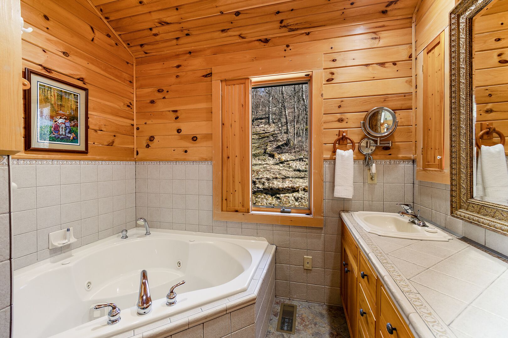Baño de cabaña de madera con una bañera grande, un lavabo y una ventana que ofrece vistas al bosque.