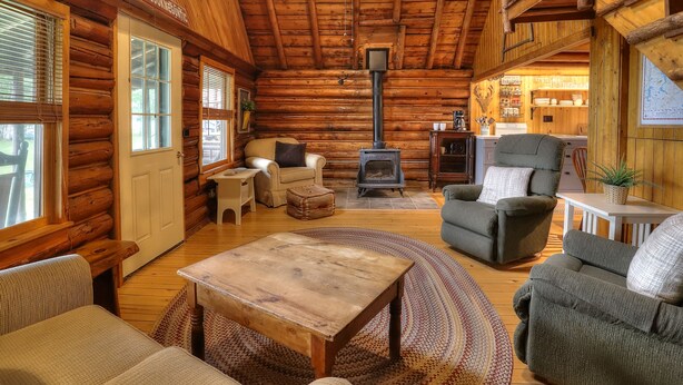 A cozy log cabin interior with a fireplace, wooden furniture, and a dining area. - 10 Haines Landing - We love this classic cabin! Pet friendly and gorgeous views!! (Oquossoc)