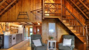 A rustic cabin interior with a kitchen, two armchairs, a small table, and a wooden staircase. - 10 Haines Landing - We love this classic cabin! Pet friendly and gorgeous views!! (Oquossoc)