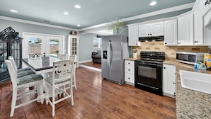 A modern kitchen with white cabinetry, a stainless steel refrigerator, a black oven, and a granite countertop. - Private Pool | Steps To Beach | Fenced Backyard | FLPCB74 (Panama City Beach)