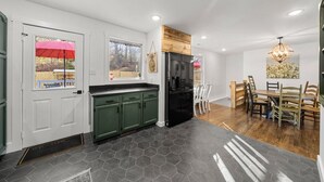 Una cocina moderna con gabinetes verdes, un refrigerador negro y un comedor con sillas de madera y una araña.