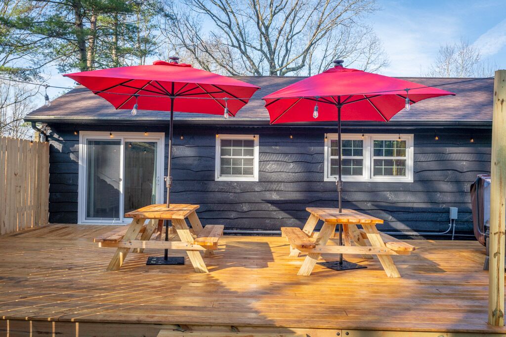 A deck with two picnic tables and two red umbrellas.