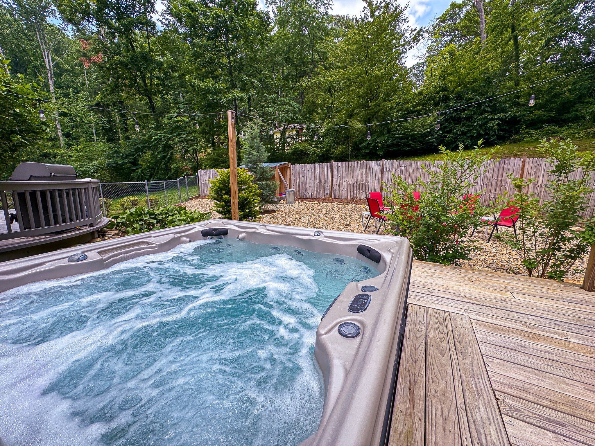 A hot tub surrounded by a wooden deck, a wooden fence, and red chairs.