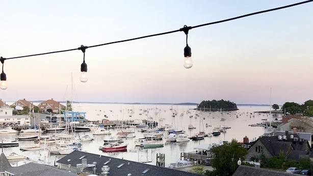 Ein Hafen mit zahlreichen vertäuten Booten, blauem Himmel und einer Lichterkette darüber.