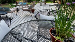 Eine Holzterrasse mit Gartenmöbeln, umgeben von Bäumen und einem Gebäude mit großen Fenstern.