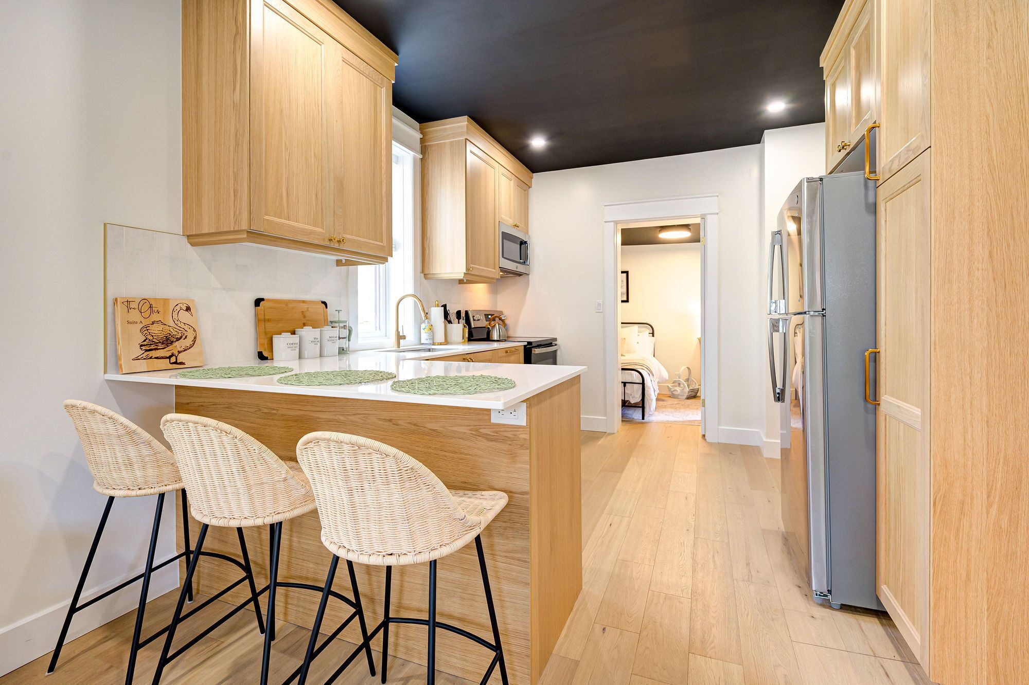 A modern kitchen with wooden cabinets, a central island with bar stools, a refrigerator, and a microwave.