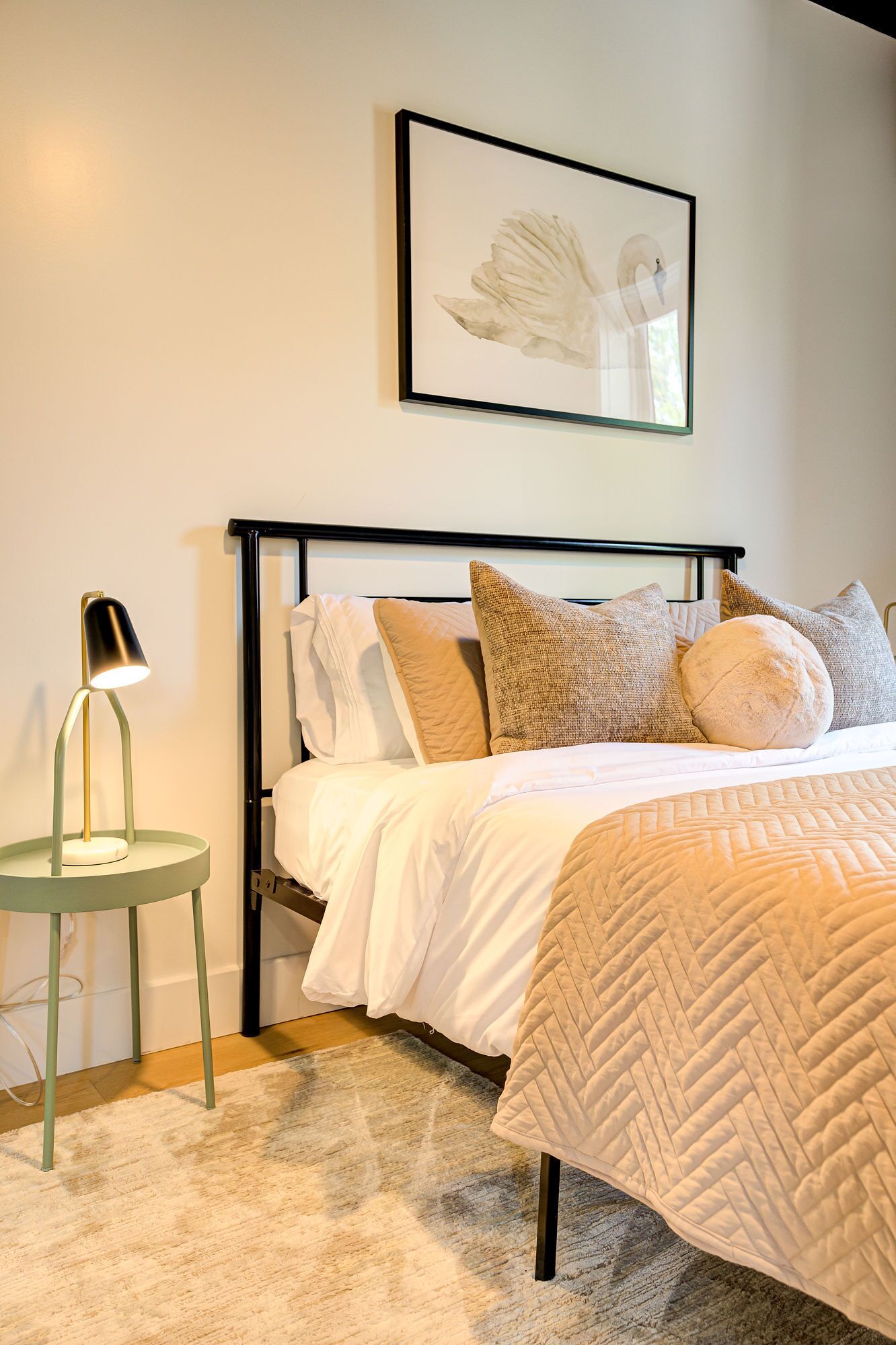 A neatly arranged bedroom with a bed, pillows, a bedside lamp, and a framed artwork on the wall.