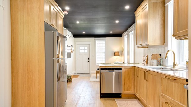 A modern kitchen with wooden cabinets, stainless steel appliances, and a black ceiling.