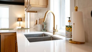 A modern kitchen with a white countertop, stainless steel sink, and a gold faucet.