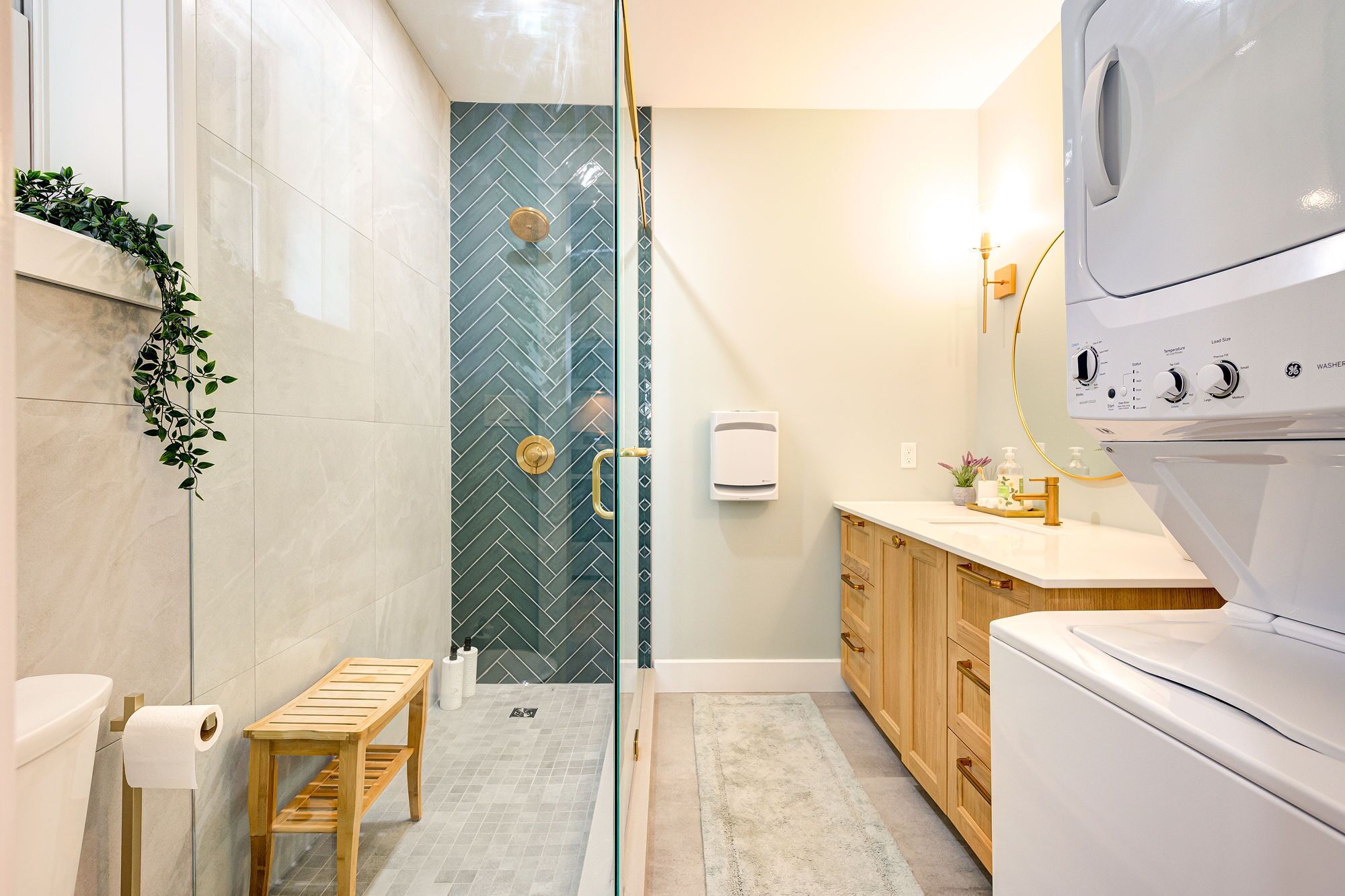 A modern bathroom with a glass shower enclosure, a wooden bench, a toilet, and a washing machine.