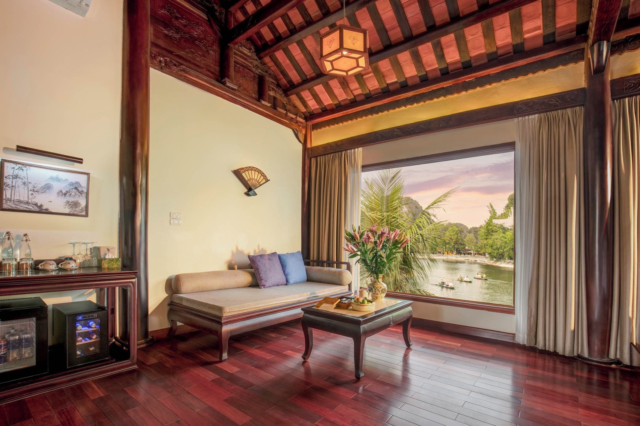 A room with a sofa, a table with a vase, a painting, and a view of a body of water.