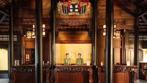 A reception area with ornate wooden furniture, a traditional Chinese altar, and two attendants. - Emeralda Resort Tam Coc (Nam Hoa Lu)