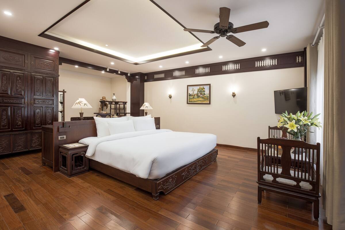 A spacious bedroom with a large bed, wooden flooring, a ceiling fan, and a TV on the wall.