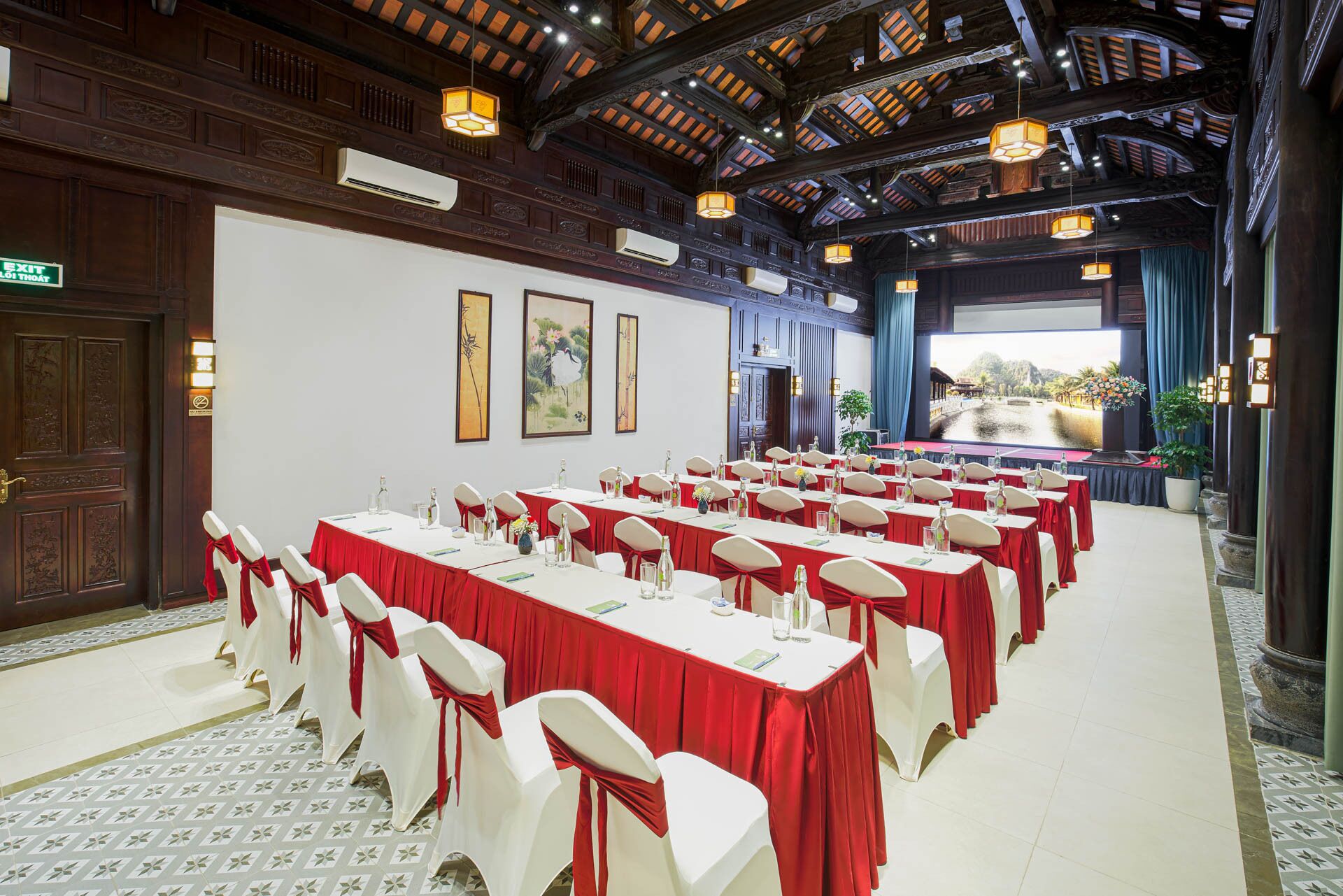 A conference room with rows of tables and chairs, a large screen, and traditional decor.