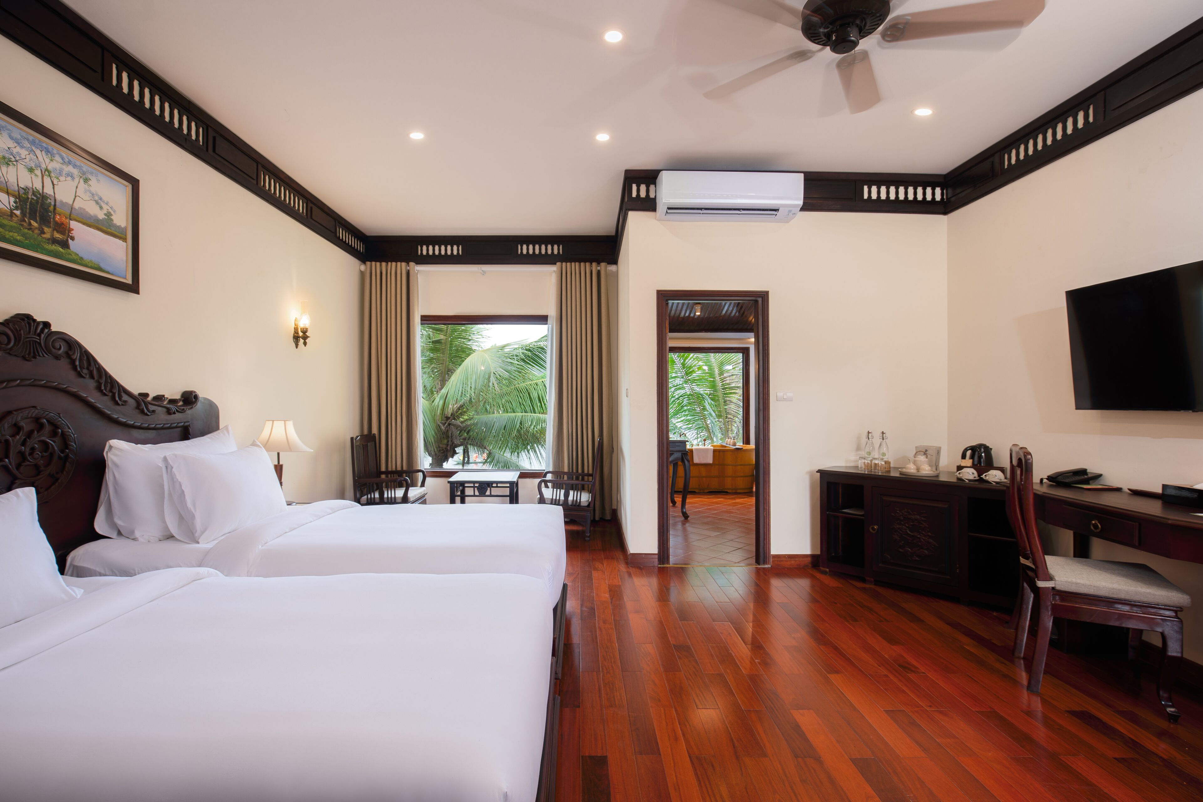 A hotel room with two beds, a desk, a chair, a television, and an air conditioning unit.