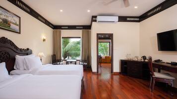 A hotel room with two beds, a desk, a chair, a television, and an air conditioning unit.