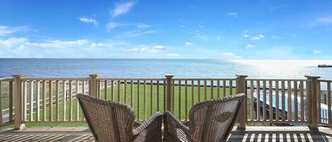 A wooden deck with wicker chairs overlooking a pool and ocean.