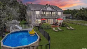 Una casa de dos pisos con piscina, tobogán y patio con mobiliario exterior.