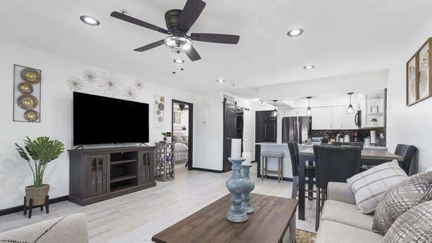 A modern living room with a flat-screen TV, a ceiling fan, and a dining area with a kitchen in the background. - Beautiful condo in Branson (Branson)
