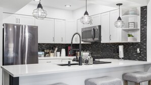 A modern kitchen with white cabinets, a stainless steel refrigerator, a black backsplash, and bar stools. - Beautiful condo in Branson (Branson)