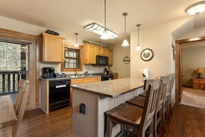 A kitchen with wooden cabinets, a central island with bar stools, a built-in microwave, and pendant lighting. - 4 King Suites | Near Silver Dollar City (Branson West)
