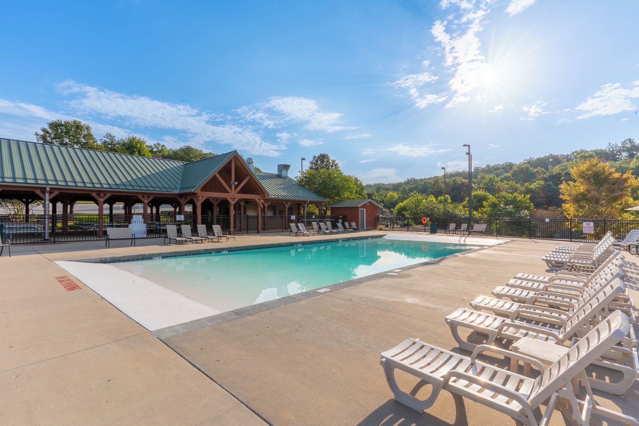 A swimming pool with lounge chairs, a covered pavilion, and a no glass allowed sign.