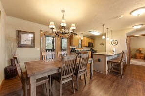 A dining area with a wooden table and chairs, a chandelier, and a kitchen in the background. - 4 King Suites | Near Silver Dollar City (Branson West)