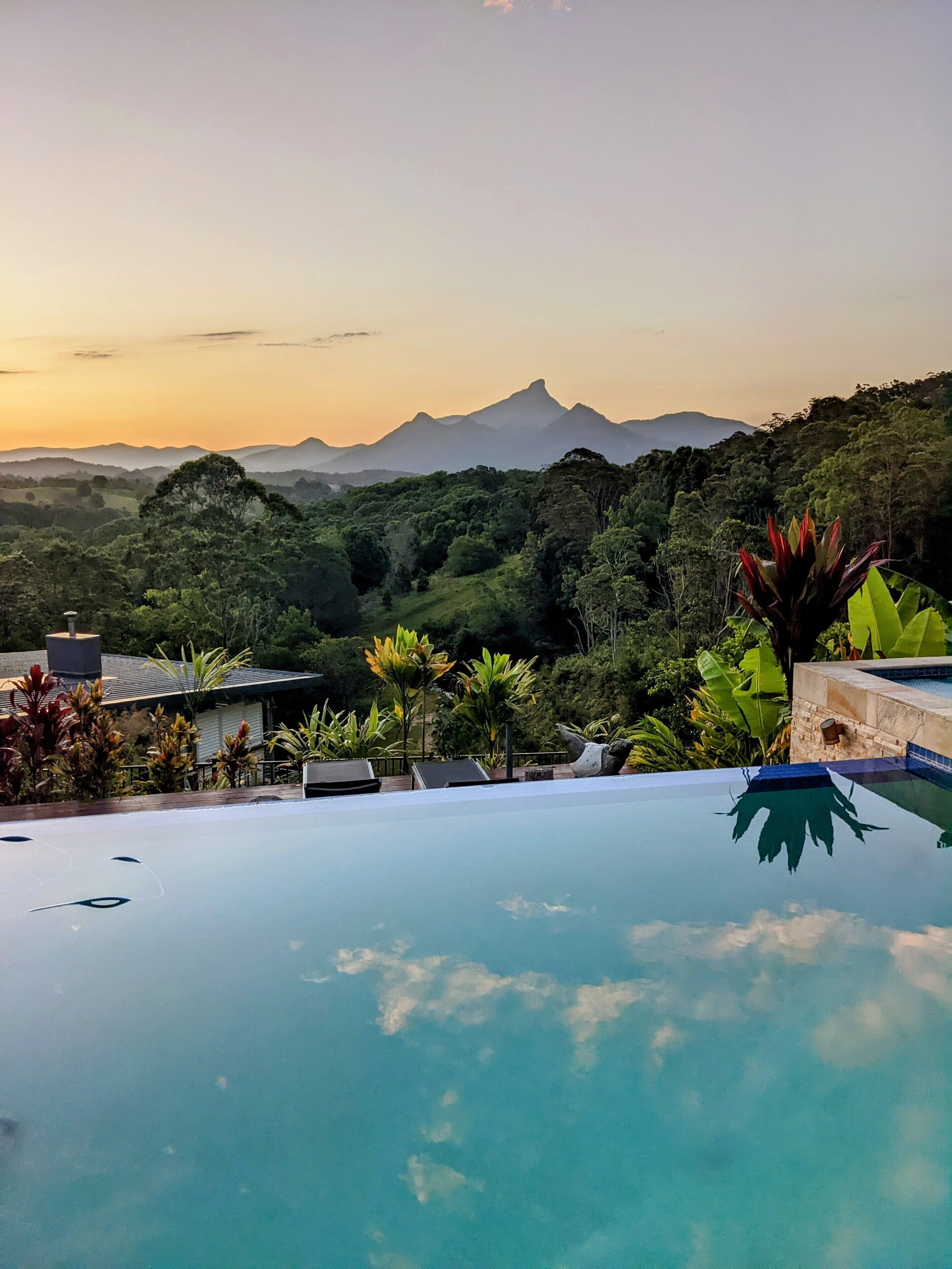 An infinity pool with a view of a mountain range and lush greenery.