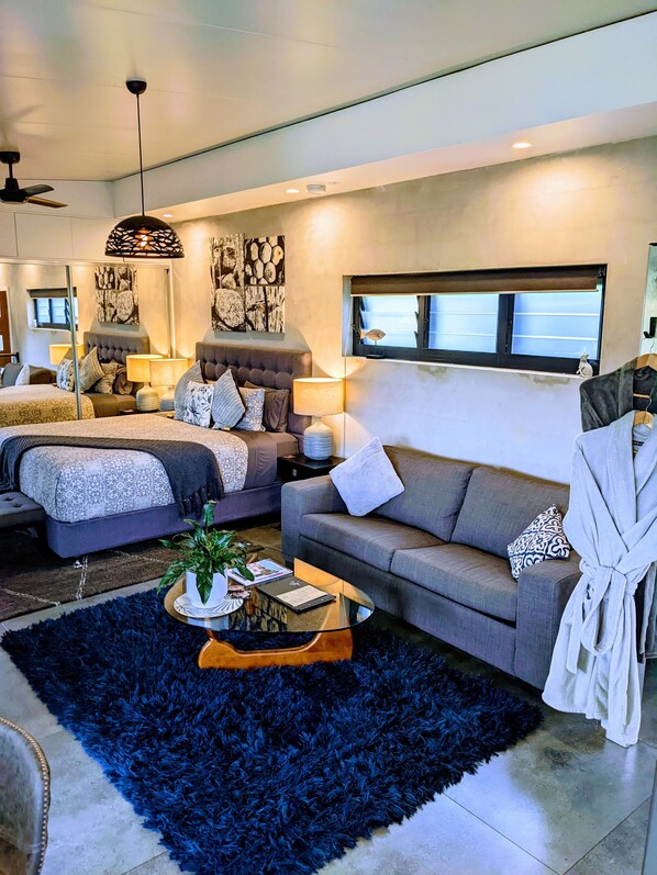 A modern hotel room with a large bed, a sofa, a coffee table, and a robe hanging on the wall. - La Rocher Eco Retreat (Smiths Creek)
