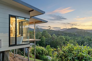 A modern house with a balcony overlooking a lush forest and hills.