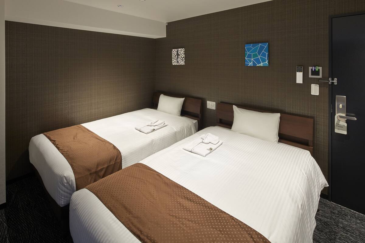 A hotel room with two beds, a door, and a wall with artwork.