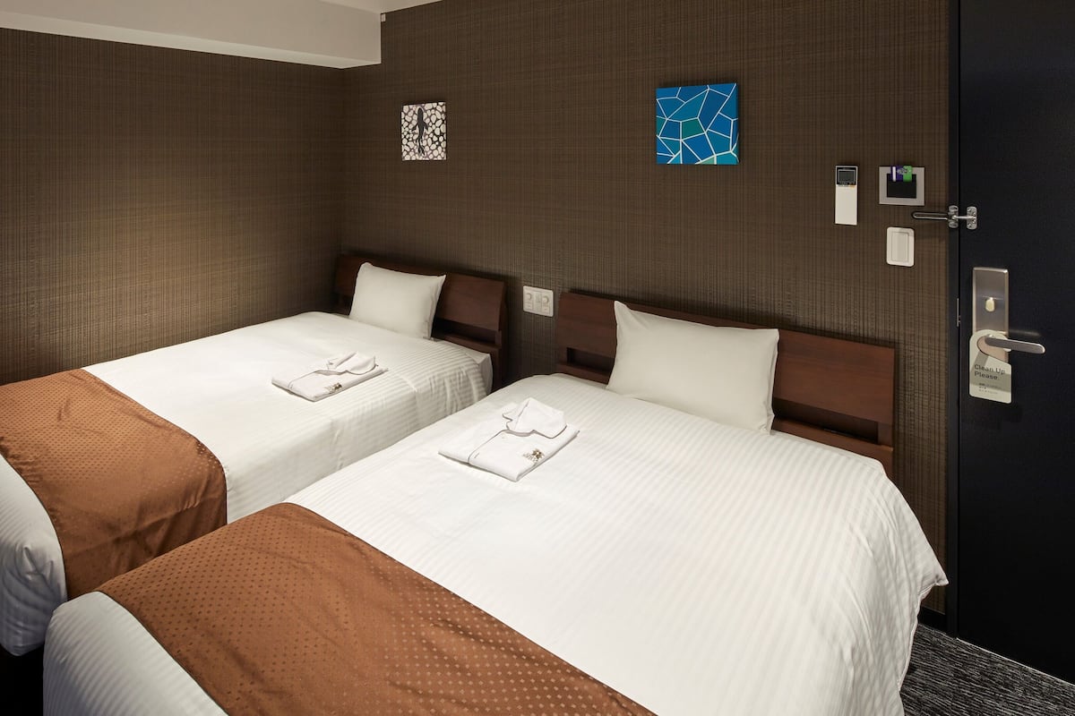 Habitación de hotel con dos camas, una puerta oscura y una pequeña obra de arte en la pared.