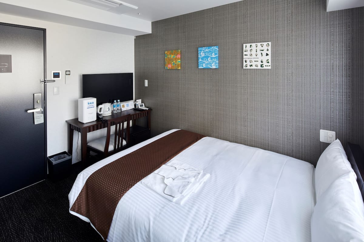 A hotel room with a neatly made bed, a desk with a coffee maker, and a wall-mounted TV.