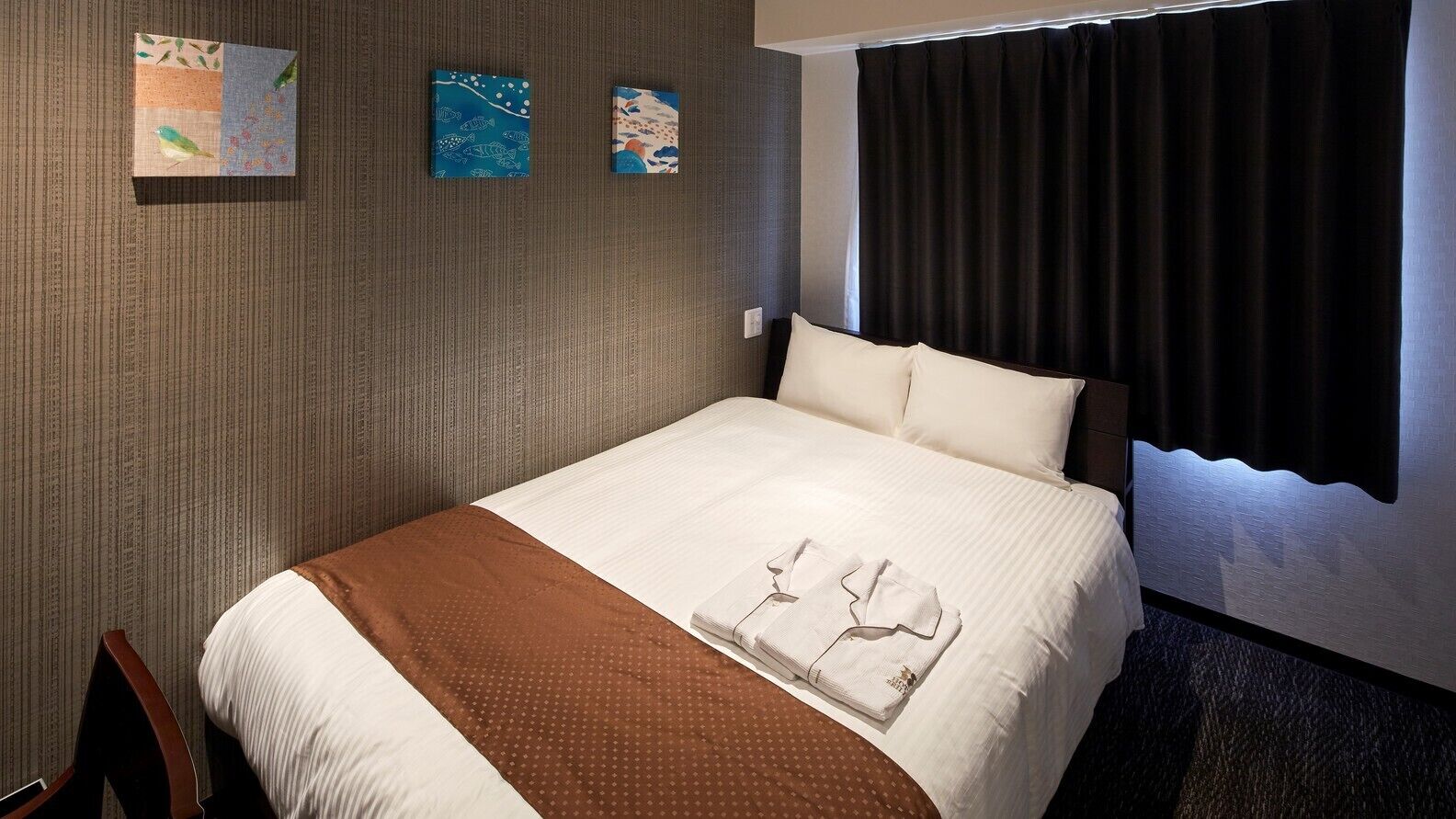 A hotel room with a bed, a brown blanket, and three wall art pieces.