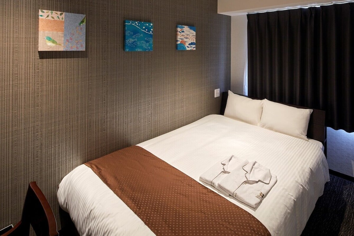 A hotel room with a bed, a brown blanket, and three wall art pieces.