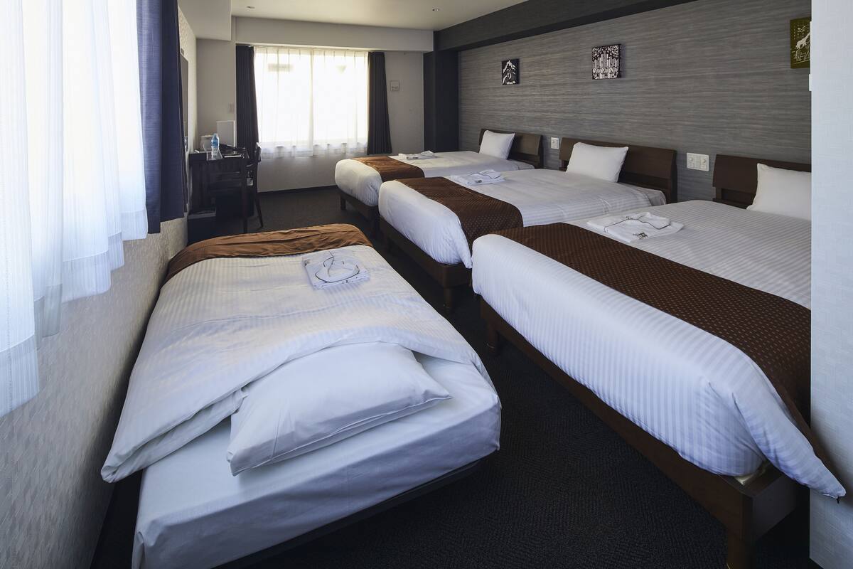 A hotel room with three single beds, a desk, and a chair.