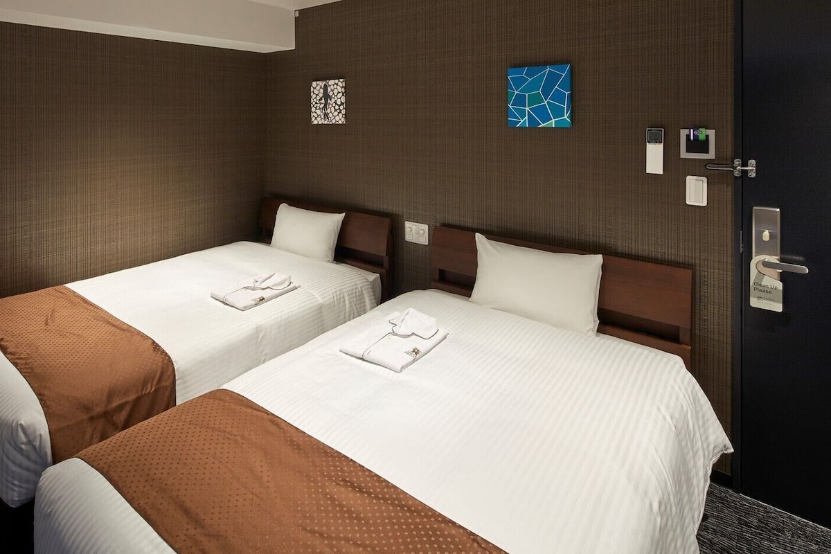 A hotel room with two beds, a dark door, and a wall clock.