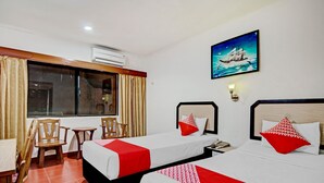 Habitación de hotel con dos camas, un escritorio, sillas y una ventana con cortinas.