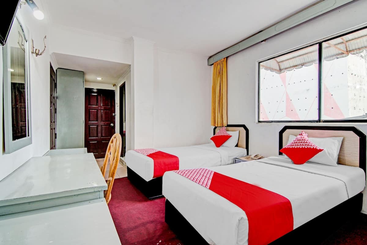 Une chambre d’hôtel avec deux lits, une petite table, un miroir et une fenêtre donnant sur un immeuble.