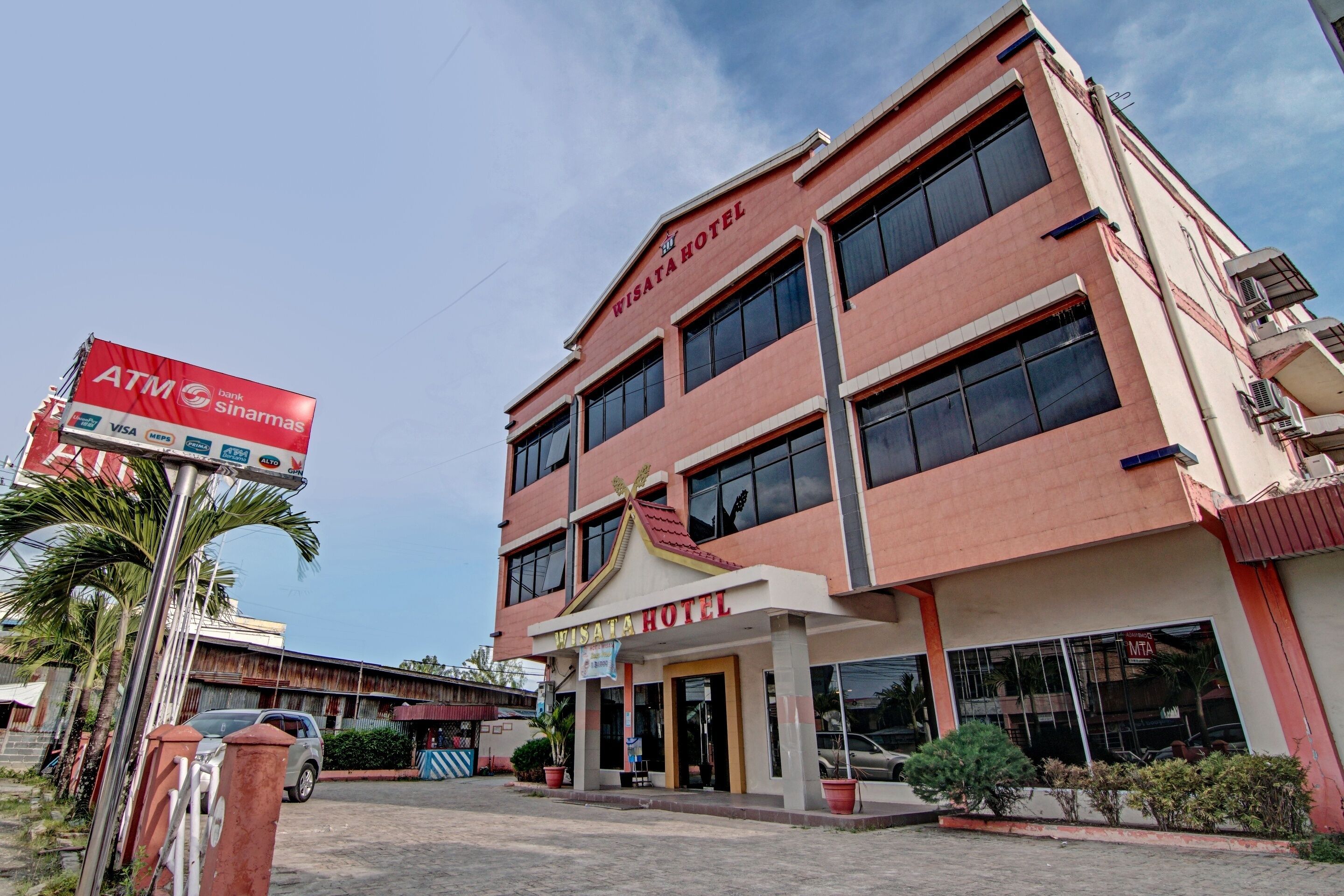 A two-story building with a sign reading "WISATA HOTEL" and an ATM sign nearby.
