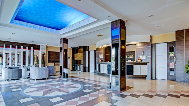 Un amplio vestíbulo con piso de diseño geométrico, una mesa de recepción y un techo decorado con un diseño que simula el cielo azul.
