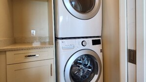 Une petite buanderie équipée de deux machines à laver à chargement frontal superposées, d’un plan de travail et d’un meuble de rangement.