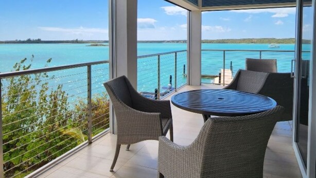 Un balcon avec une table ronde et des chaises, d’où l’on peut admirer une mer turquoise et une terre lointaine.