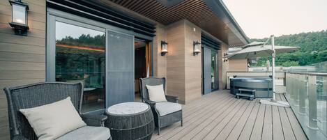 Terraza moderna al aire libre con mobiliario de mimbre, jacuzzi y barandilla de vidrio con vistas panorámicas.